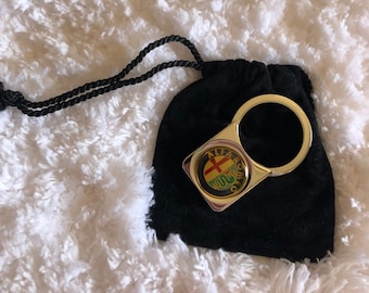 May include: A gold-colored key chain with a black velvet pouch. The key chain features the Alfa Romeo logo with a red cross and a green snake.