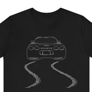 May include: Black t-shirt featuring a white outline of a Corvette sports car driving on a road with tyre tracks behind it.