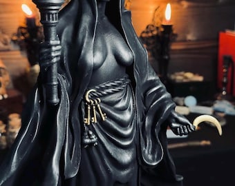 May include: A matte black statue of a crowned figure wearing a blindfold and draped robes. The figure holds a gold-colored torch in one hand and a small crescent moon in the other. A rope belt secures three gold-colored keys at the waist.