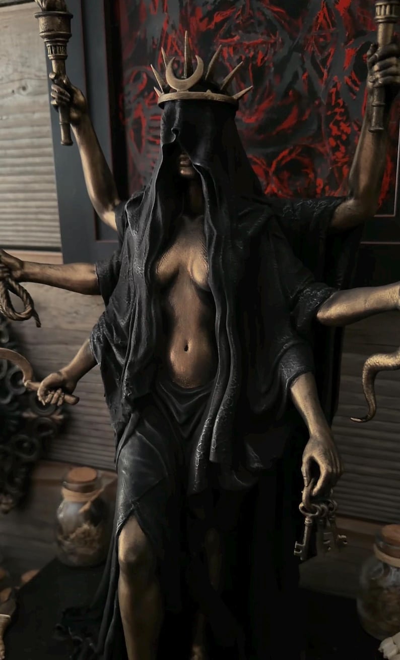 May include: A multi-armed bronze-toned statue of a figure wearing a black hooded cloak and a crown with a crescent moon. The figure holds two torches, a rope, a curved blade, and a set of keys in its six hands. The statue features a dark finish.