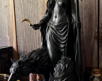 Könnte beinhalten: Schwarze Statue einer bekleideten Figur mit goldener Krone und Fackel, die eine Sichel hält, flankiert von zwei Wolfsfiguren. Die Statue steht auf einer schwarzen Truhe vor einem hölzernen Hintergrund.