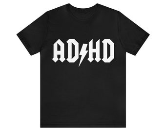 Peut inclure: T-shirt noir avec un graphique blanc qui dit "ADHD" dans une police de caractères rock and roll avec un éclair.