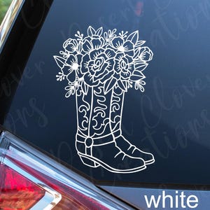 May include: White vinyl decal showing a pair of cowboy boots filled with flowers. The boots have decorative stitching and are filled with a variety of floral elements. The word "white" is printed at the bottom.