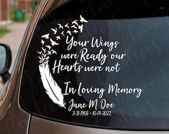 Op de afbeelding: Een witte vinyl sticker op een achterruit van een auto met een veer die overgaat in een zwerm vogels. De tekst luidt: Your Wings were Ready our Hearts were not, In Loving Memory, Jane M Doe, 3-31-1958 - 10-14-2022.