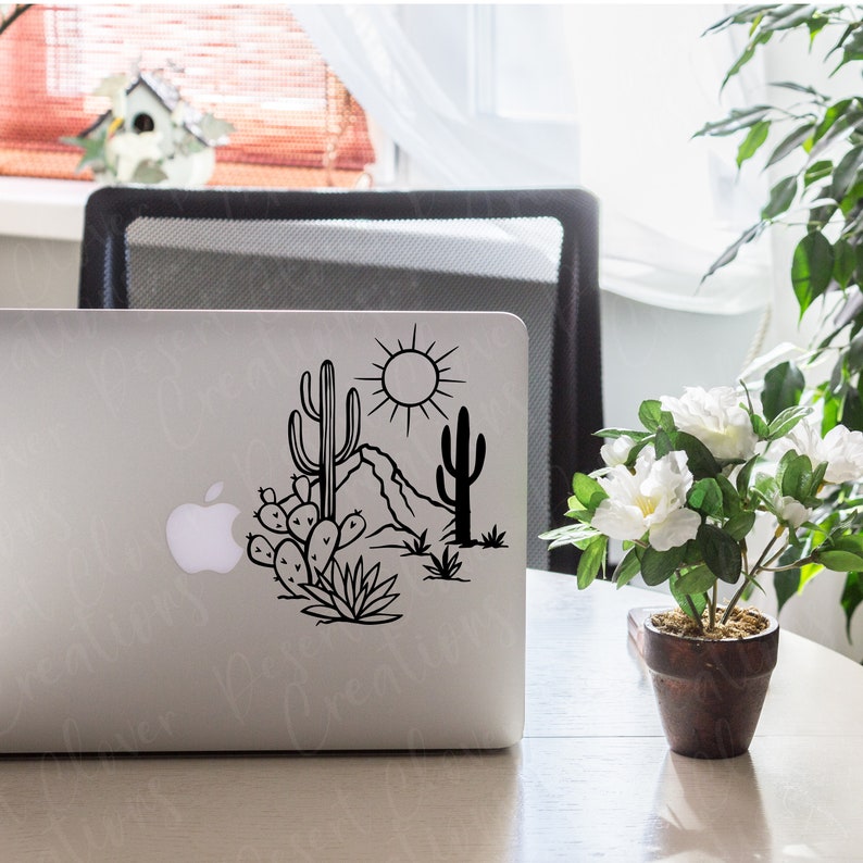 May include: A black and white illustration of a desert landscape with cacti, a mountain, and a sun. The illustration is on a silver laptop.