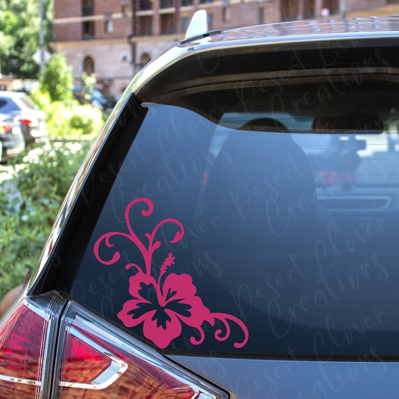 May include: Pink hibiscus flower decal with a swirling vine design. The decal is applied to the back window of a car.