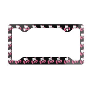 May include: A rectangular license plate frame featuring a repeating pattern of the white Hello Kitty character with a pink bow against a solid black background. The frame includes four circular mounting holes positioned at the corners.