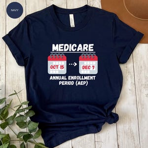 May include: Navy blue t-shirt with white text and calendar graphics. The text reads "MEDICARE" above two calendar icons with the dates "OCT 15" and "DEC 7". Below the calendars is the text "ANNUAL ENROLLMENT PERIOD (AEP)".