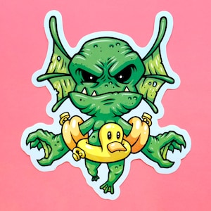 May include: A green cartoon monster with a grumpy expression is wearing a yellow rubber ducky floatie. The monster has large, pointed ears and sharp teeth.