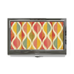 May include: A rectangular metal business card holder featuring a glossy finish and a repeating pattern of vertical wavy lines in shades of mustard yellow, sage green, and coral red, separated by thin cream-colored curves on a dark metallic frame.
