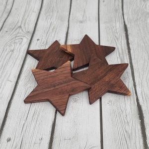 Puede incluir: Cuatro posavasos de madera en forma de estrella hechos de madera de nogal oscuro. Los posavasos están apilados, con las puntas de las estrellas superpuestas.