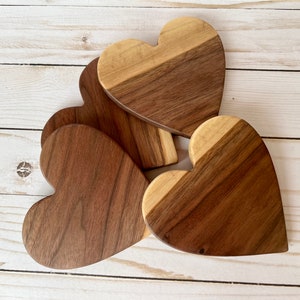 May include: A collection of heart-shaped wooden coasters. Each coaster is crafted from two tones of wood, with a light and dark brown color scheme. The coasters are arranged on a light-colored wooden surface.