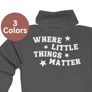 Pode incluir: Uma camisola de capuz cinzenta escura com o texto "WHERE LITTLE THINGS MATTER" em branco com estrelas de cada lado de cada palavra.