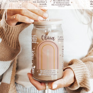 May include: A glass tumbler with a wooden lid and straw, featuring a design with the name "Olivia" and a rainbow arch. The tumbler has inspirational text and Bible verses printed on it. The words "lid & straw included" are also visible.