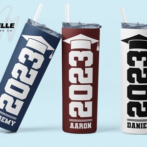 May include: Three stainless steel tumblers with graduation caps and the year 2023 printed on them. The tumblers are in navy blue, maroon, and white with black text. The names Jeremy, Aaron, and Daniel are printed on the bottom of each tumbler.