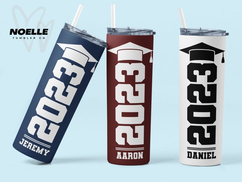 May include: Three stainless steel tumblers with graduation caps and the year 2023 printed on them. The tumblers are in navy blue, maroon, and white with black text. The names Jeremy, Aaron, and Daniel are printed on the bottom of each tumbler.