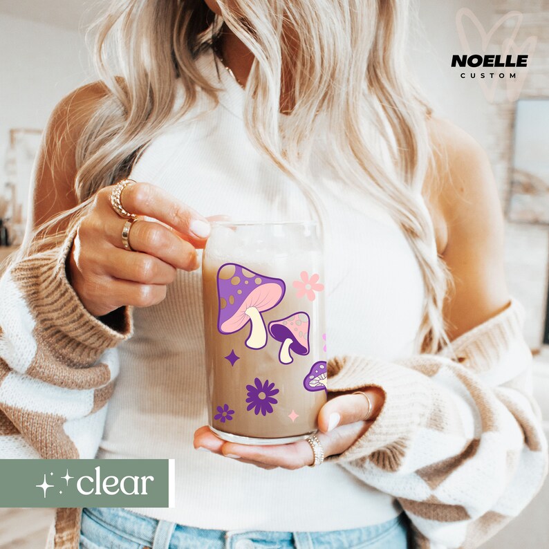 May include: A clear glass with a brown liquid and purple and pink mushroom illustrations. The glass has a white background with purple flowers and stars.