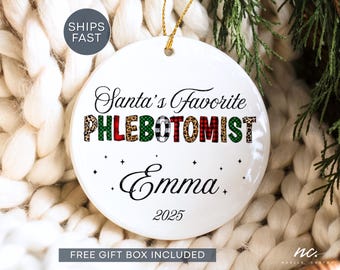 May include: A round white ceramic ornament featuring the black text Santa's Favorite PHLEBOTOMIST with letters filled in leopard print and red and green plaid patterns. Below, the name Emma is printed in black script with the year 2025.