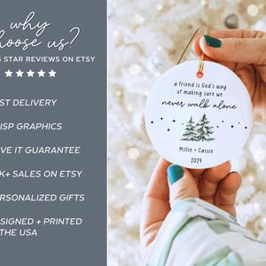 May include: A round white ceramic ornament featuring the text 'a friend is God's way of making sure we never walk alone', a green pine tree illustration, and the names 'Millie + Cassie' with the year '2024' printed in black ink.