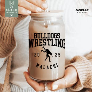 May include: A clear glass jar with a brown lid and a straw. The jar has a black and white graphic that says "Bulldogs Wrestling" with a wrestler silhouette and the numbers "20" and "25". The text "Malachi" is below the graphic.