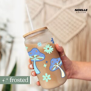 May include: A frosted glass tumbler with a brown lid and a straw. The tumbler has a design of blue and white mushrooms and flowers. The text "frosted" is visible in the lower left corner of the image.