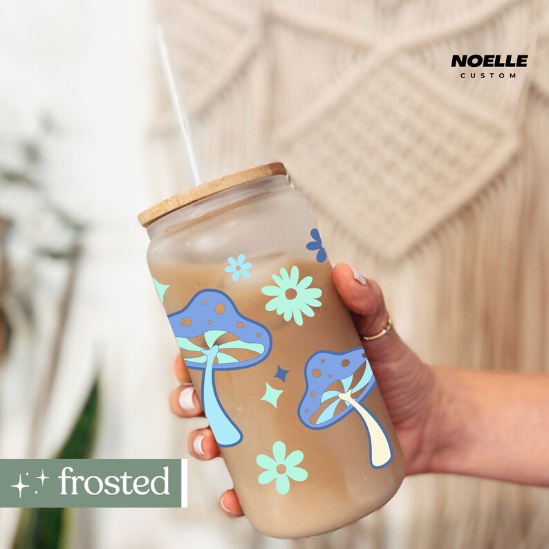 May include: A frosted glass tumbler with a brown lid and a straw. The tumbler has a design of blue and white mushrooms and flowers. The text "frosted" is visible in the lower left corner of the image.