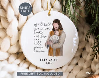 May include: A round white ceramic ornament featuring a watercolor illustration of a figure holding a baby. The text reads: We'll hold you in our hearts until we can hold you in heaven. BABY SMITH 2026 is printed below the illustration.