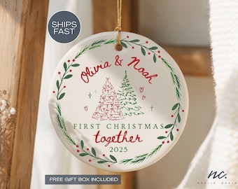 May include: A round, white Christmas ornament with the names "Olivia & Noah" in red script. It features two Christmas trees, hearts, and the text "FIRST CHRISTMAS together 2025" in red. A green and red leaf border encircles the design.