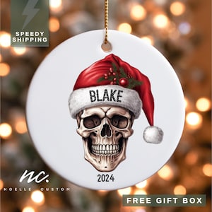 May include: White ceramic Christmas ornament with a skull wearing a red Santa hat. The hat has the name "BLAKE" on it and the year "2024" is printed below the skull.