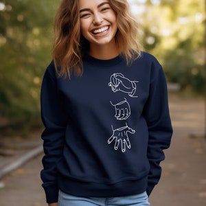 May include: A navy blue sweatshirt with a white outline of three hands in different positions. The hands are arranged vertically on the front of the sweatshirt.
