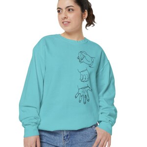 May include: A turquoise blue sweatshirt with a black line drawing of three hands on the front.