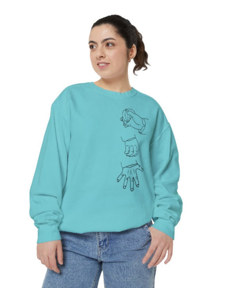 May include: A turquoise blue sweatshirt with a black line drawing of three hands on the front.