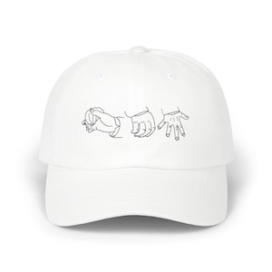 May include: White baseball cap featuring a black line art illustration of three hands in different gestures. The cap has a curved brim and a rounded crown. The design is centered on the front of the cap.