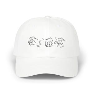 Peut inclure: Casquette de baseball blanche avec un dessin au trait noir de trois mains dans différentes positions sur le devant.