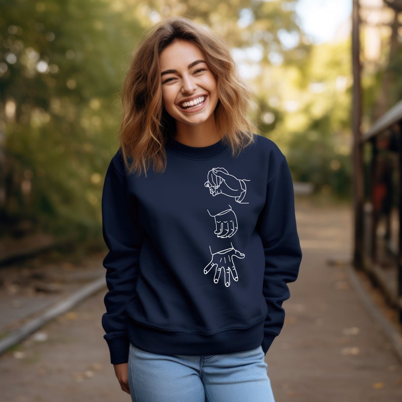 May include: A navy blue sweatshirt with a white outline of three hands in different positions. The hands are arranged vertically on the front of the sweatshirt.