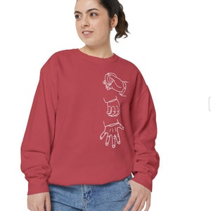 May include: A red sweatshirt with a white outline of three hands making different signs. The hands are in a vertical line on the front of the sweatshirt.
