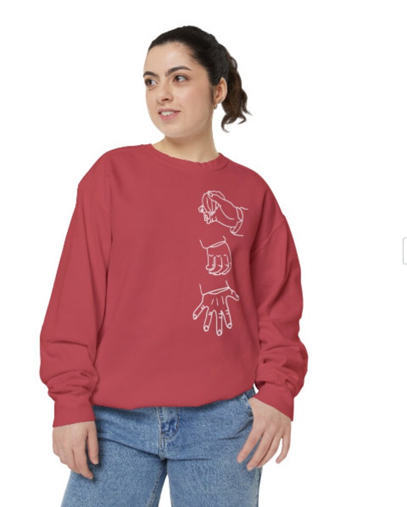 May include: A red sweatshirt with a white outline of three hands making different signs. The hands are in a vertical line on the front of the sweatshirt.
