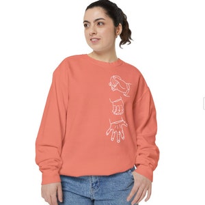 May include: A coral colored sweatshirt with a white outline of three hands in different positions.