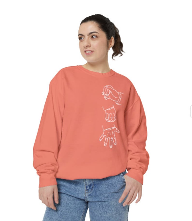 May include: A coral colored sweatshirt with a white outline of three hands in different positions.