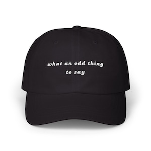 May include: Black baseball cap with white embroidered text that reads "what an odd thing to say".
