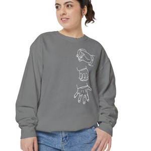 May include: A gray sweatshirt with a white outline of three hands in different positions. The hands are stylized and appear to be reaching out or interacting with each other.