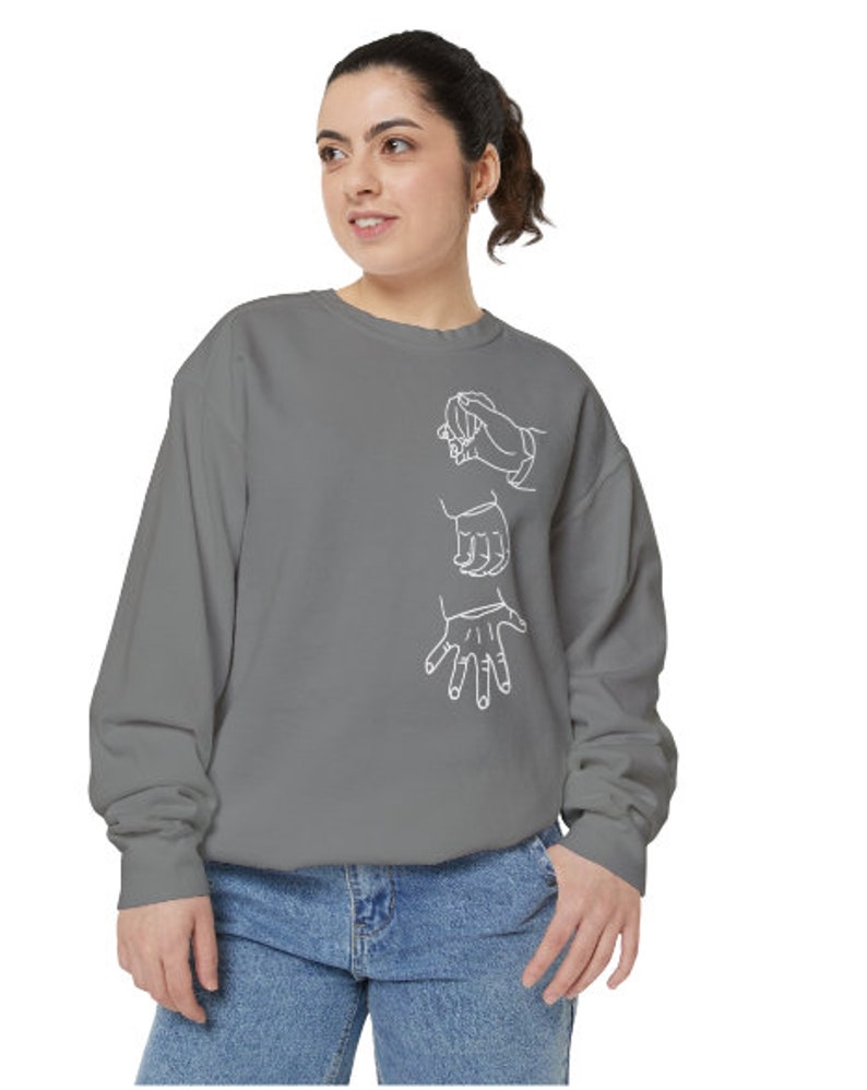 May include: A gray sweatshirt with a white outline of three hands in different positions. The hands are stylized and appear to be reaching out or interacting with each other.