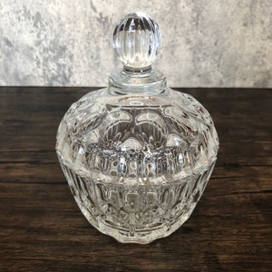 May include: A clear glass candy dish with a decorative knob on the lid. The dish has a textured, faceted design.