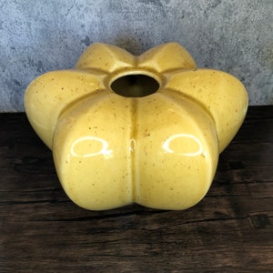 Puede incluir: Un jarrón de cerámica amarillo con forma de flor y un esmalte moteado.