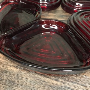 May include: Set of six ruby red glass heart-shaped dishes. The dishes are made of clear glass with a deep red tint. The dishes are perfect for serving snacks, appetizers, or desserts.