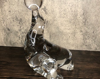 May include: A clear glass sculpture of a seal balancing a ball on its nose. The sculpture is detailed and realistic, capturing the playful nature of the animal.