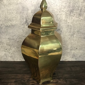 May include: A gold metal decorative vase with a pointed lid. The vase has a geometric shape and a shiny finish.