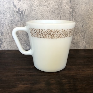 Puede incluir: Taza de cerámica blanca con un diseño floral marrón alrededor del borde superior.