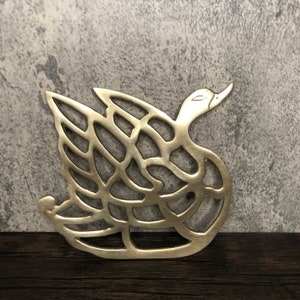 May include: A gold metal swan-shaped trivet with a decorative, intricate design. The trivet is a decorative home accent.