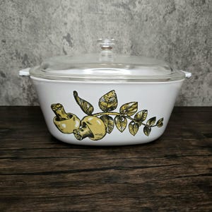 May include: White casserole dish with a glass lid featuring a yellow and green mushroom and leaf design.
